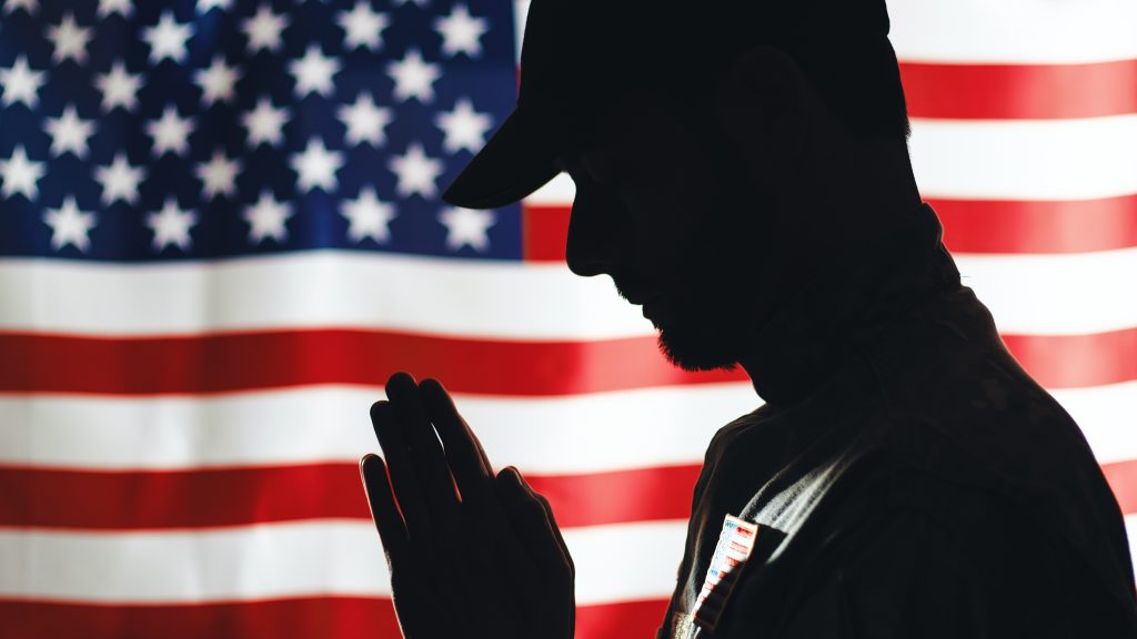 American soldier praying in front of the United States flag — symbol of faith, sacrifice, and national prayer on 9/11.