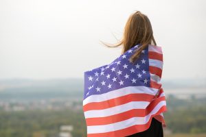 Young woman holding the American flag outdoors — symbol of hope, freedom, and unity in America.
